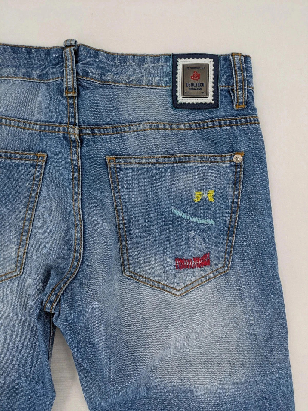 Andrew & Angel blue straight jeans distressed with red tartan patches and worn details.
