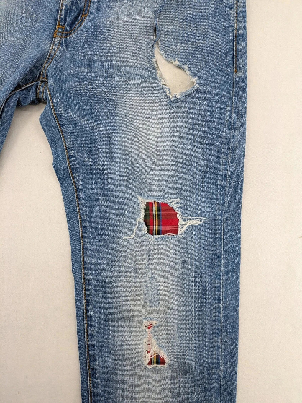 Andrew & Angel blue straight jeans distressed with red tartan patches and worn details.