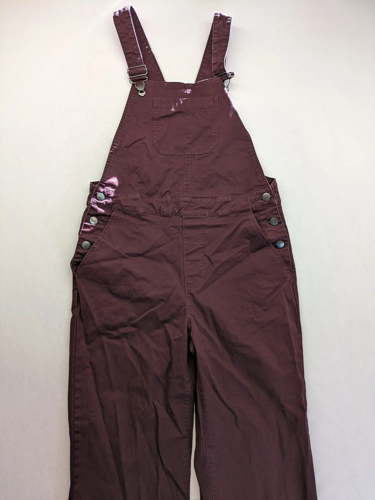 Kazane burgundy overalls with adjustable straps, side button placket, and chest pocket.