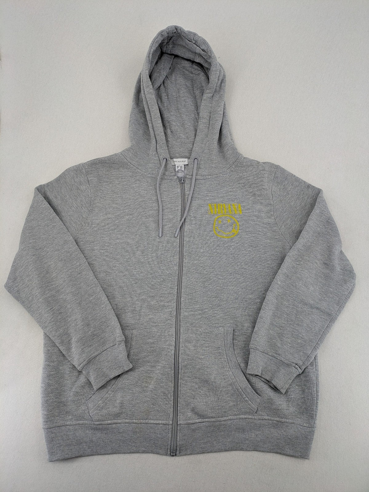 Primark grey zip-through hoodie featuring yellow Smiley logo and Nevermind graphic.