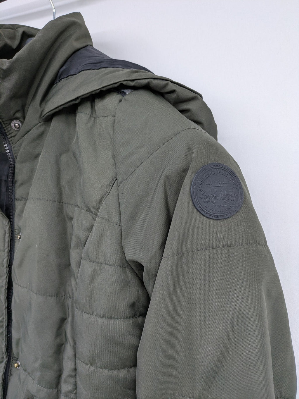 Vero Moda green puffer coat with quilted design and hood, featuring zipper and button closure.