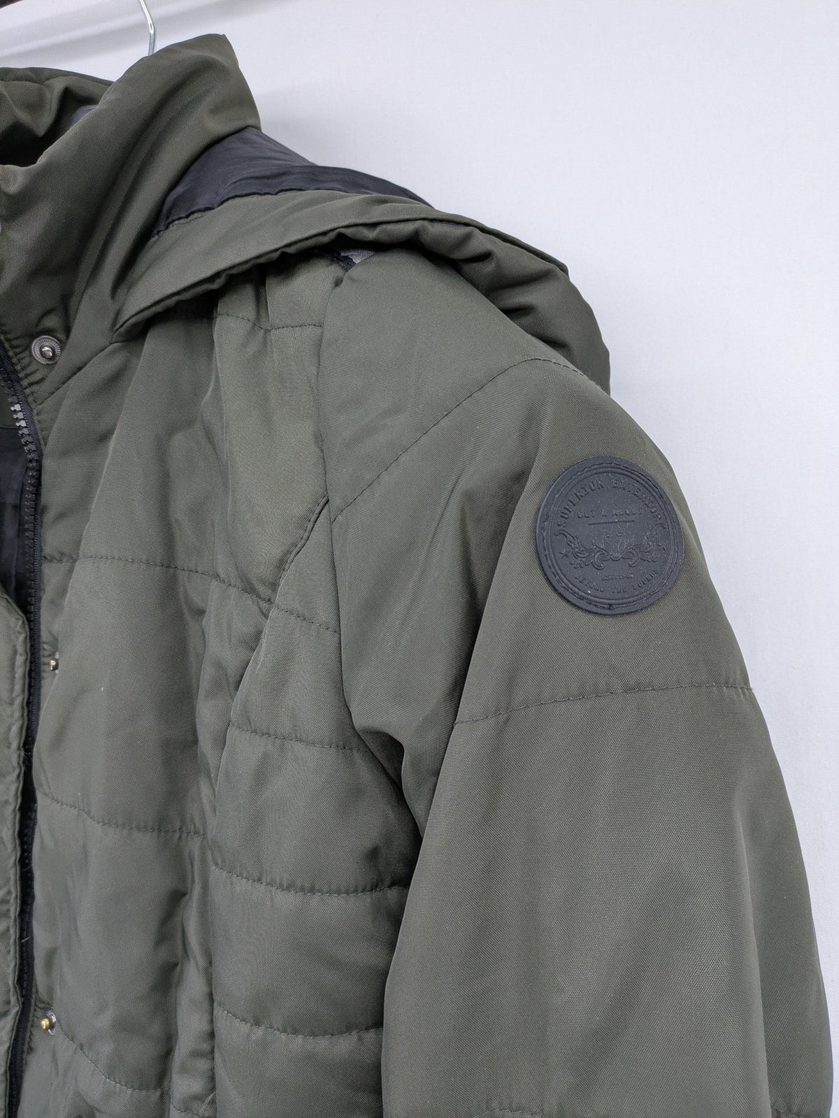 Vero Moda green puffer coat with quilted design and hood, featuring zipper and button closure.