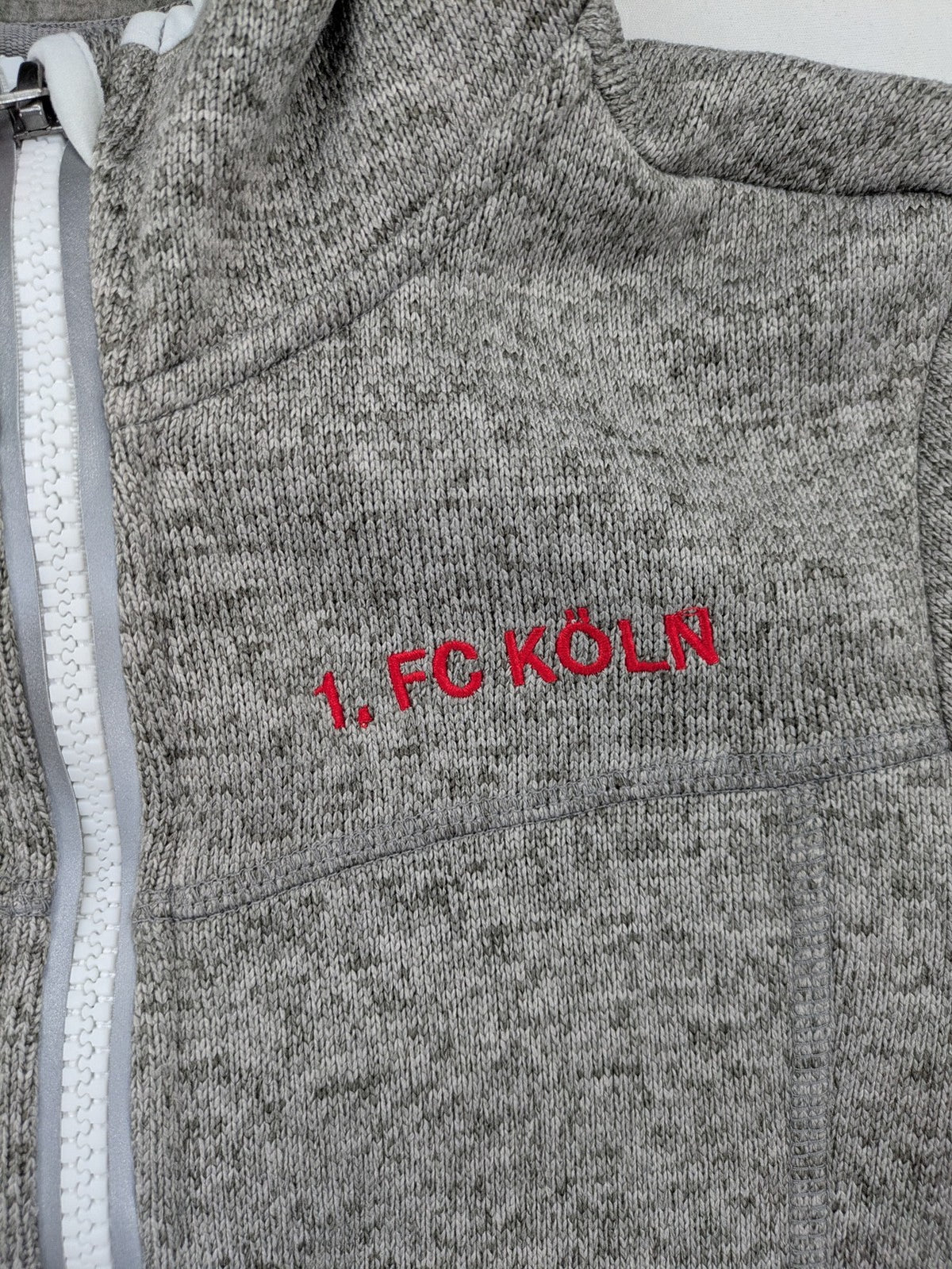 1. FC Köln grey fleece jacket with embroidered logo and hood, perfect for fans.