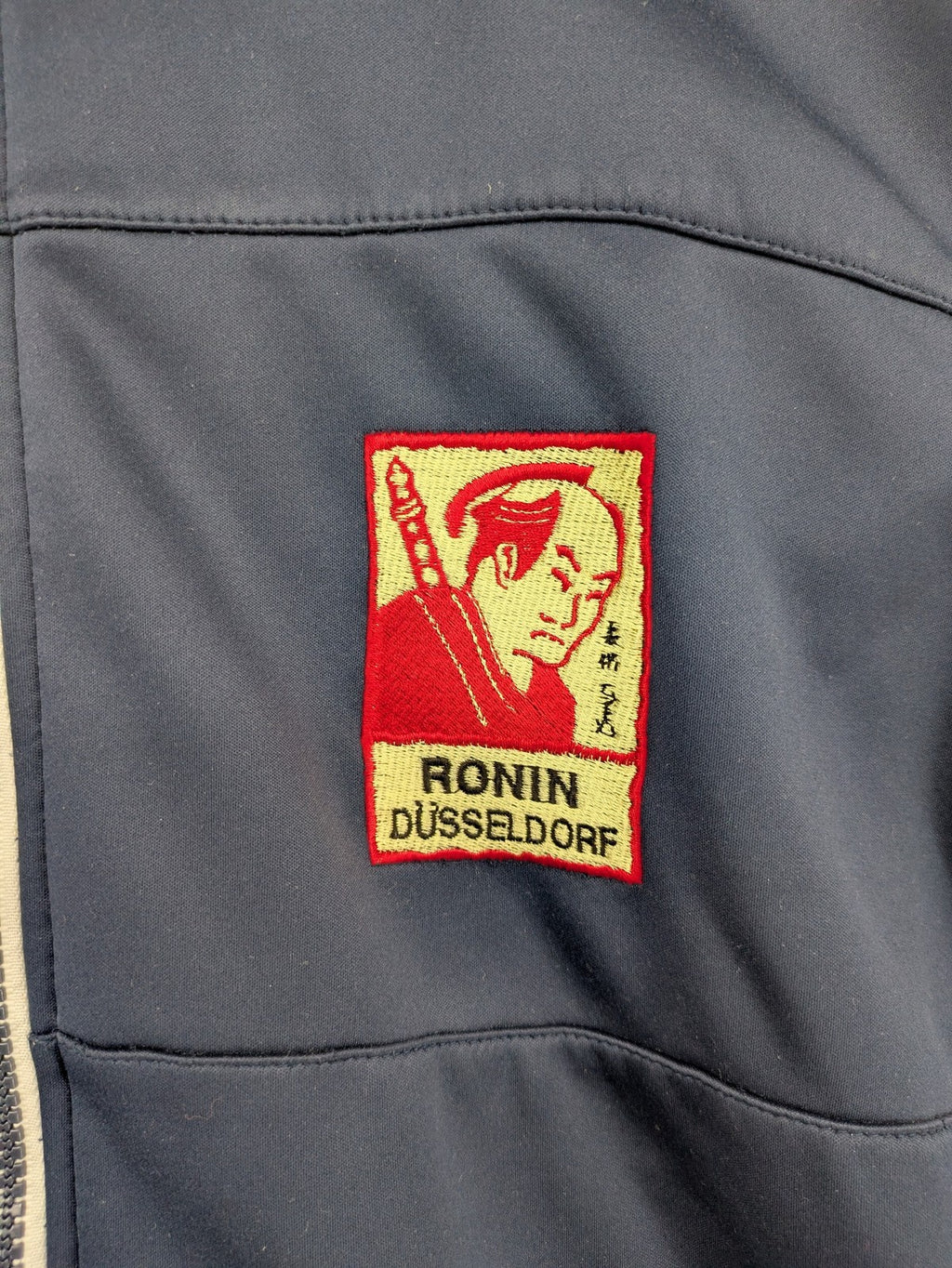 James & Nicholson beige softshell jacket with fleece lining and embroidered Ronin Düsseldorf patch.