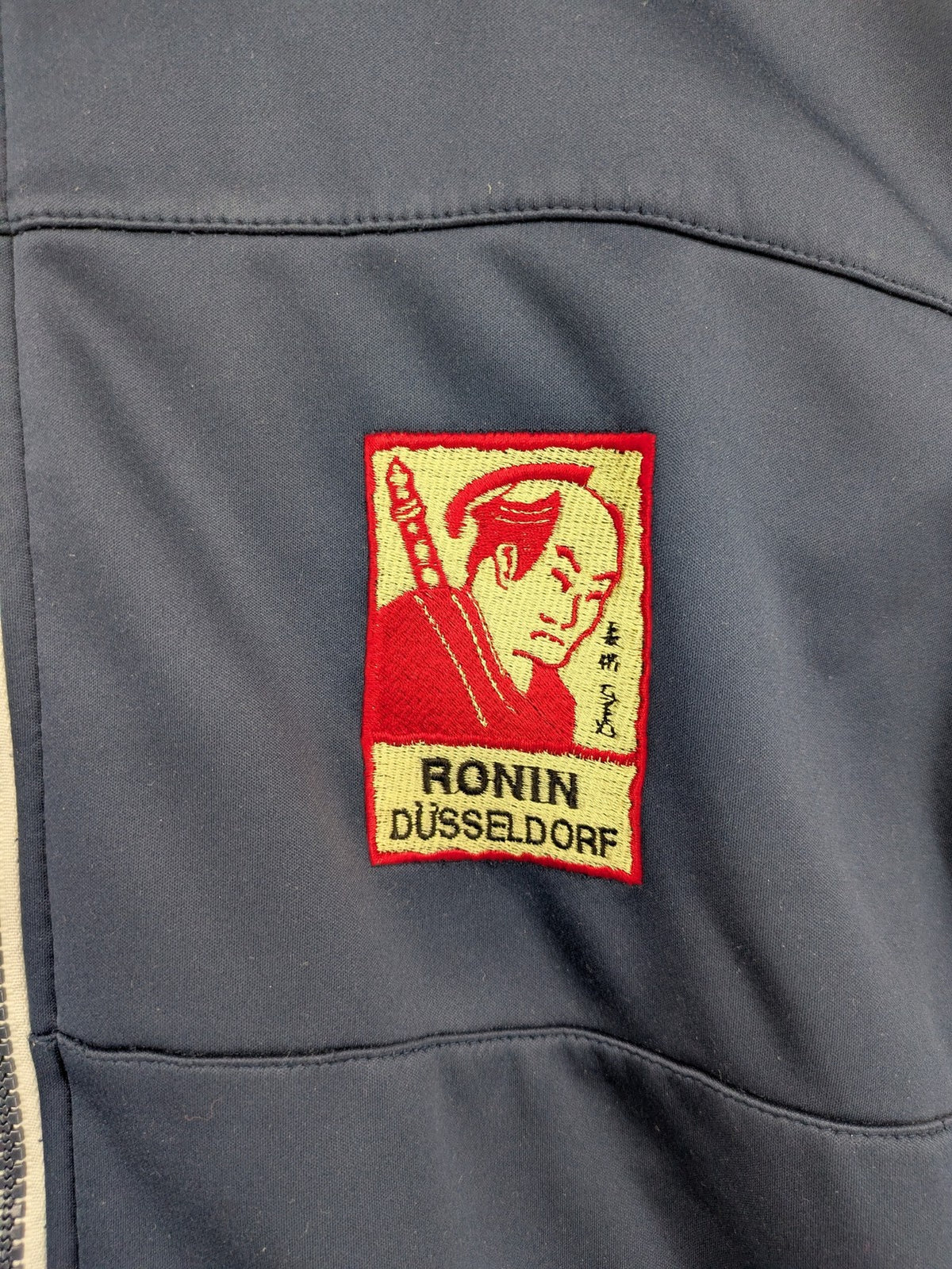 James & Nicholson beige softshell jacket with fleece lining and embroidered Ronin Düsseldorf patch.