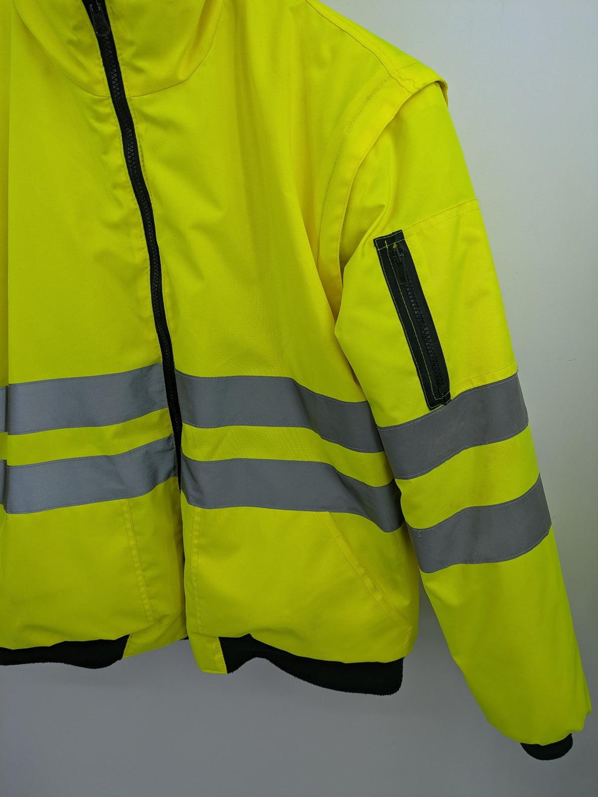 Hüren OHG grey and neon yellow safety jacket with reflective stripes and zippered arm pocket.