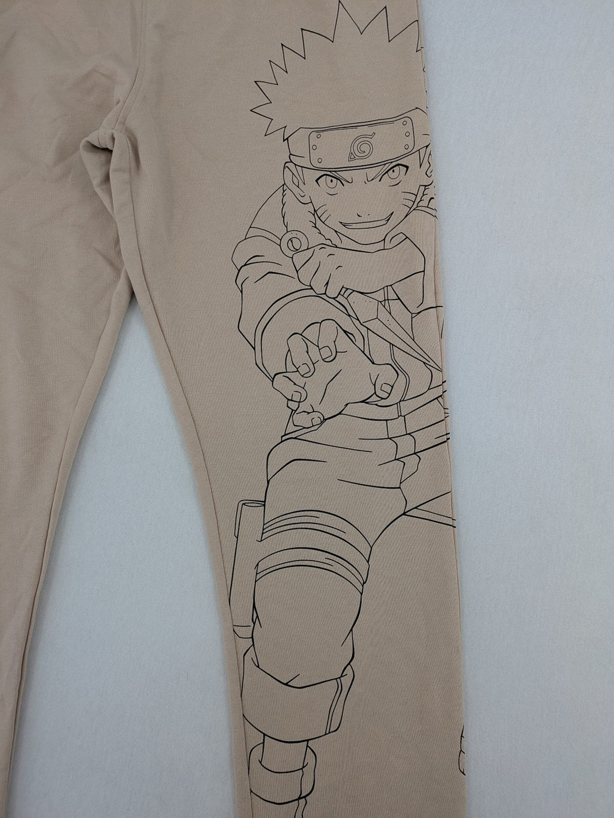 Naruto Shippuden beige joggers featuring Naruto Uzumaki graphic and logo print.
