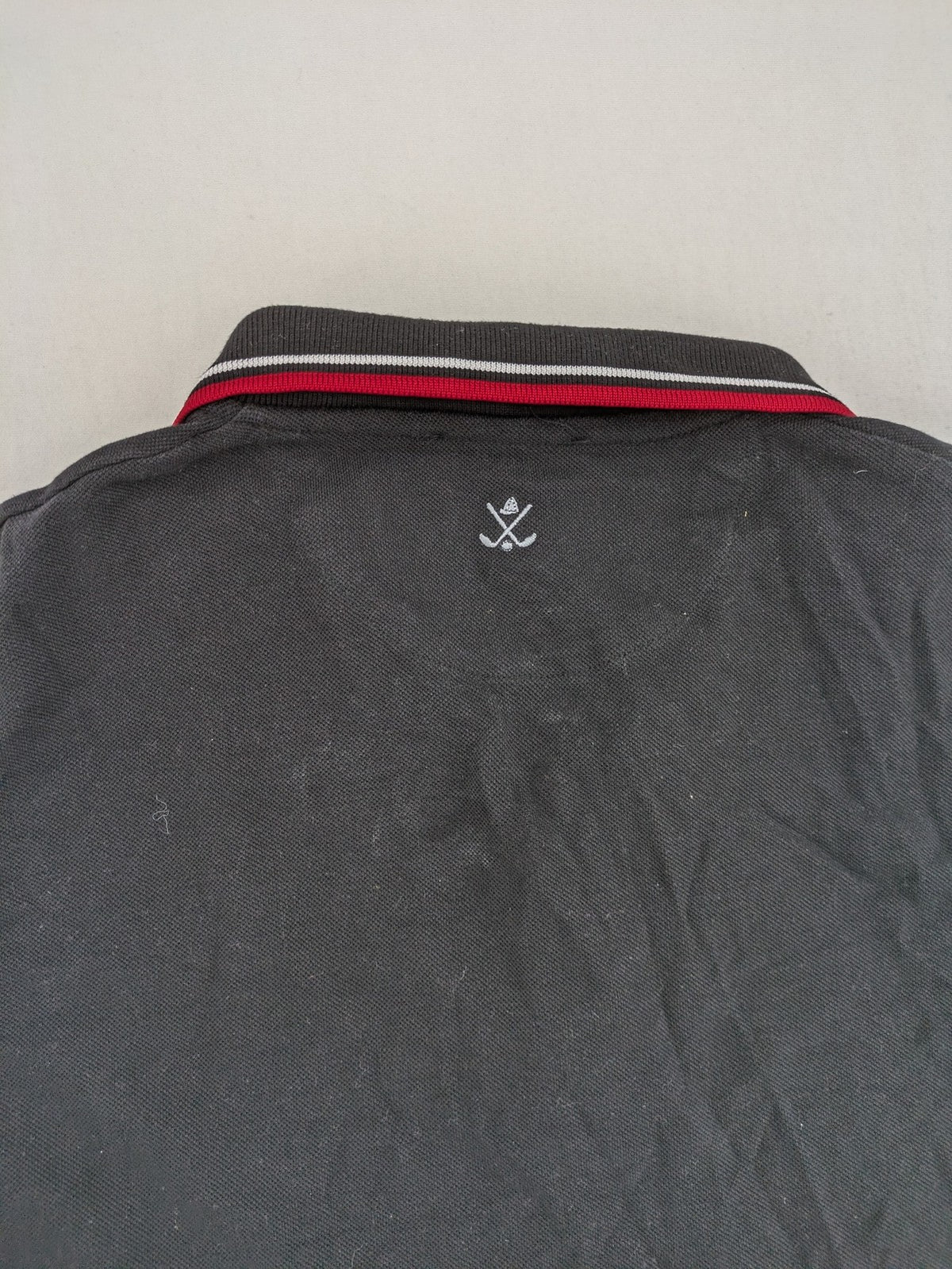 Sir Raymond Tailor black polo shirt with red and white striped collar, embroidered golfer logo.
