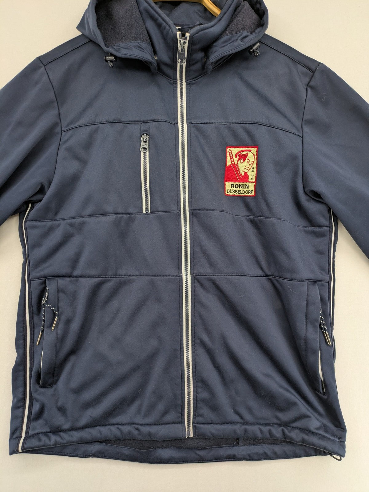 James & Nicholson beige softshell jacket with fleece lining and embroidered Ronin Düsseldorf patch.