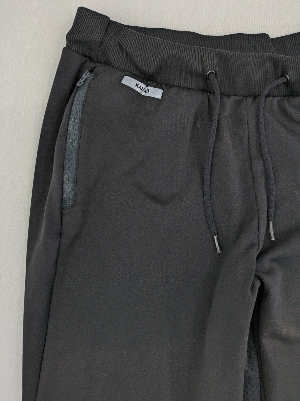 Kalenji black loungewear pants with grey accents and zippered side pockets.