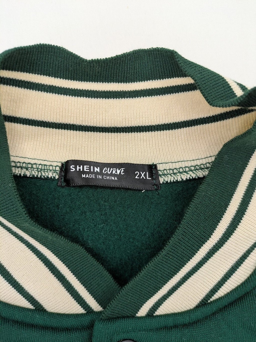 Shein Curve beige bomber jacket with green "Alaska" embroidery and striped ribbed cuffs.