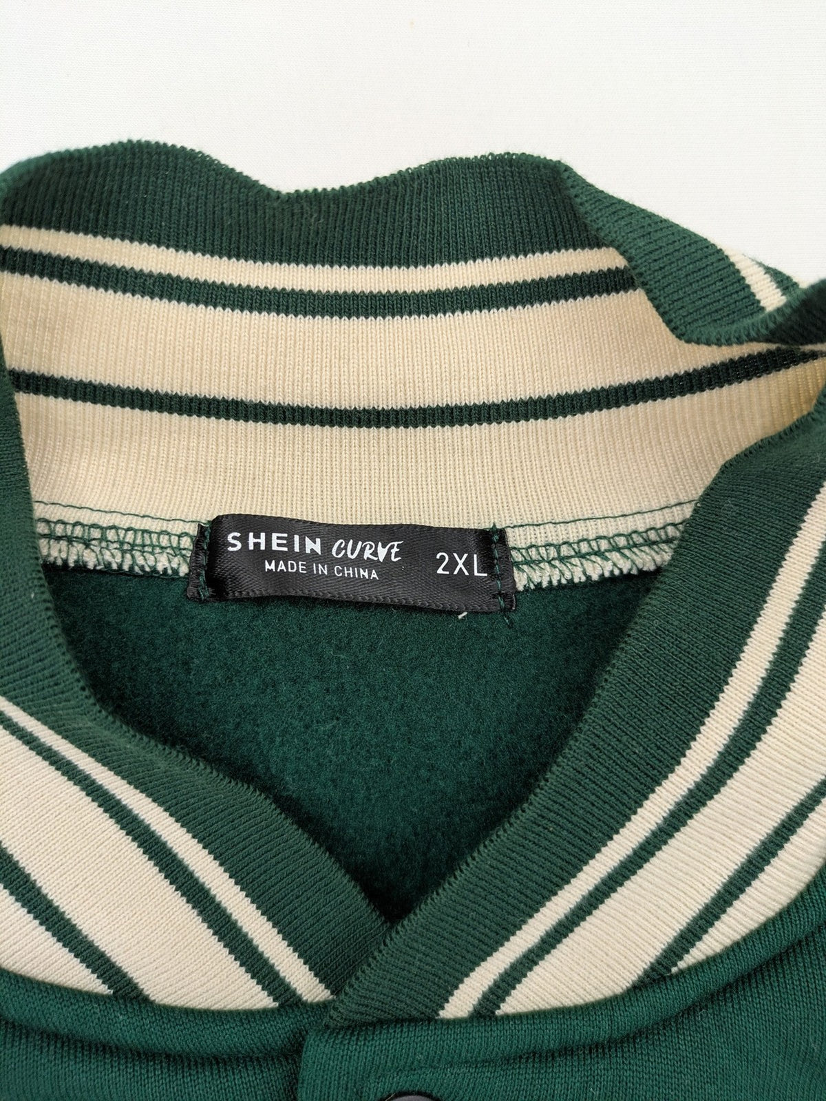 Shein Curve beige bomber jacket with green "Alaska" embroidery and striped ribbed cuffs.