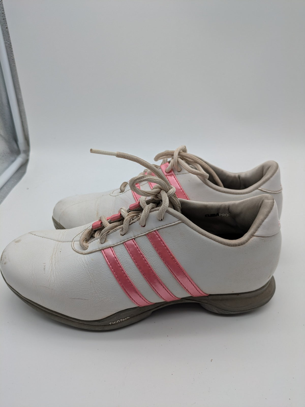 Adidas white golf shoes with pink stripes, Thintech and TRAXION technology, stylish design.