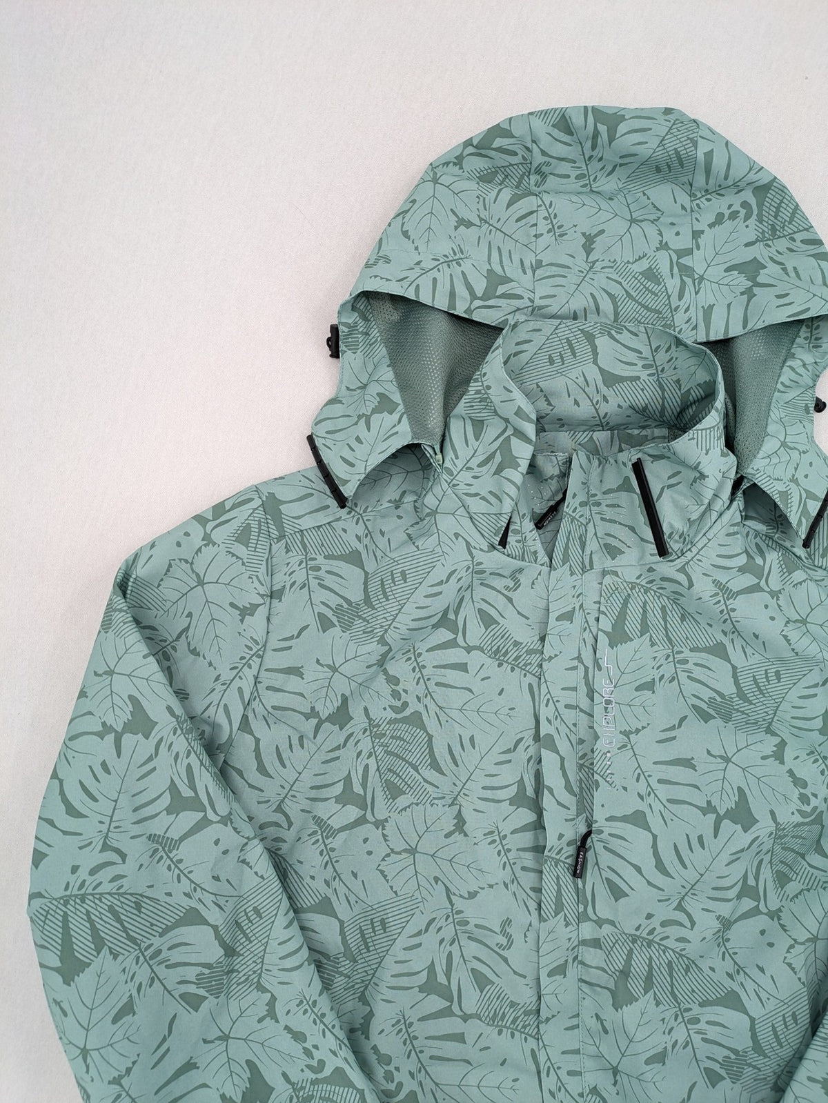Outdoor green jacket with allover leaf print, adjustable hood, and front zipper.