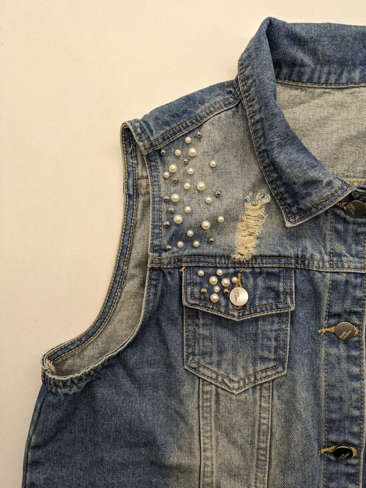 Damen Jeansjacke blau ärmellos mit Perlenverzierung, distressed Details und Knopfleiste.