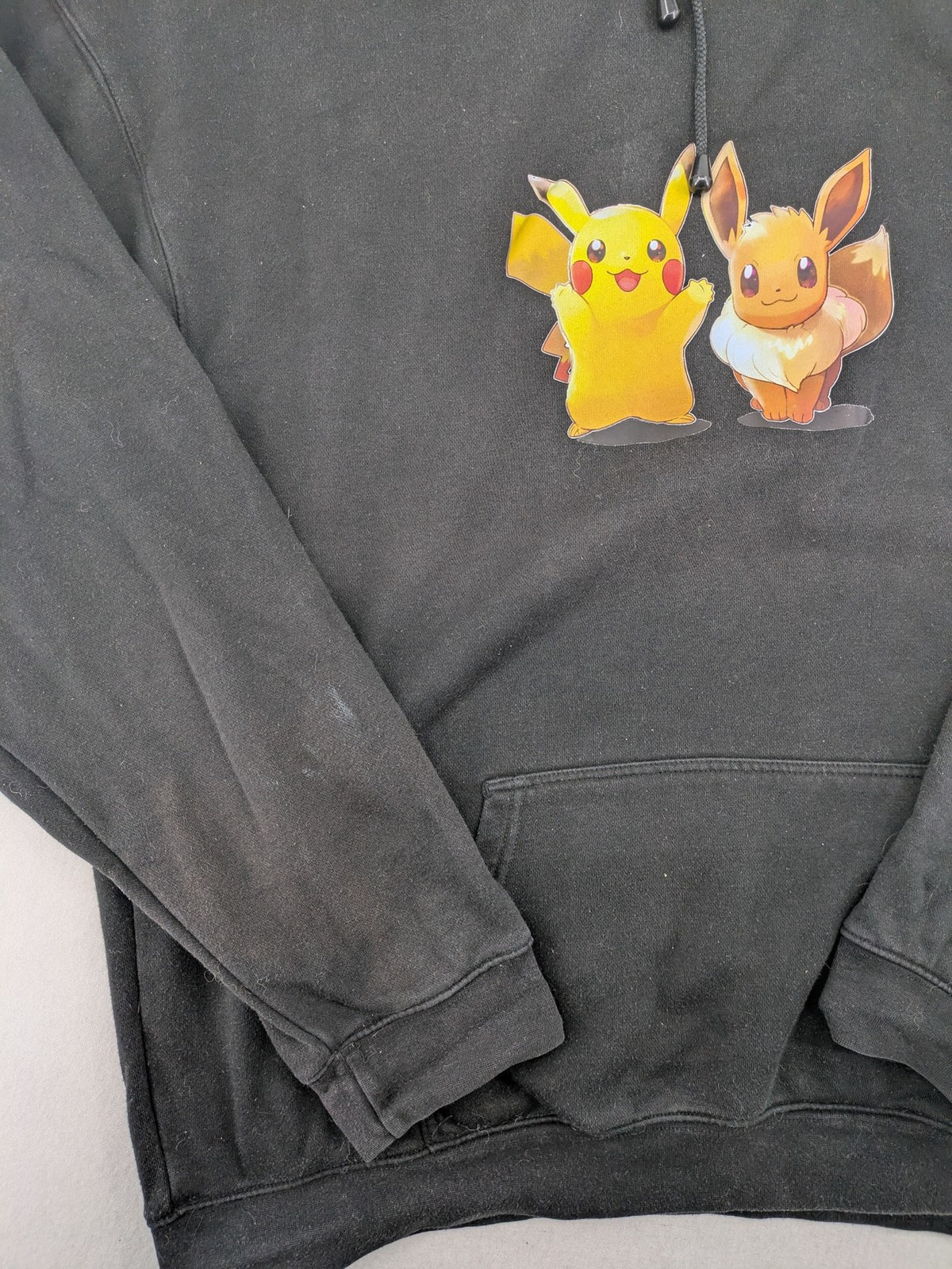 Pokémon black hoodie featuring colorful Pikachu and Evoli graphic, classic pullover style.