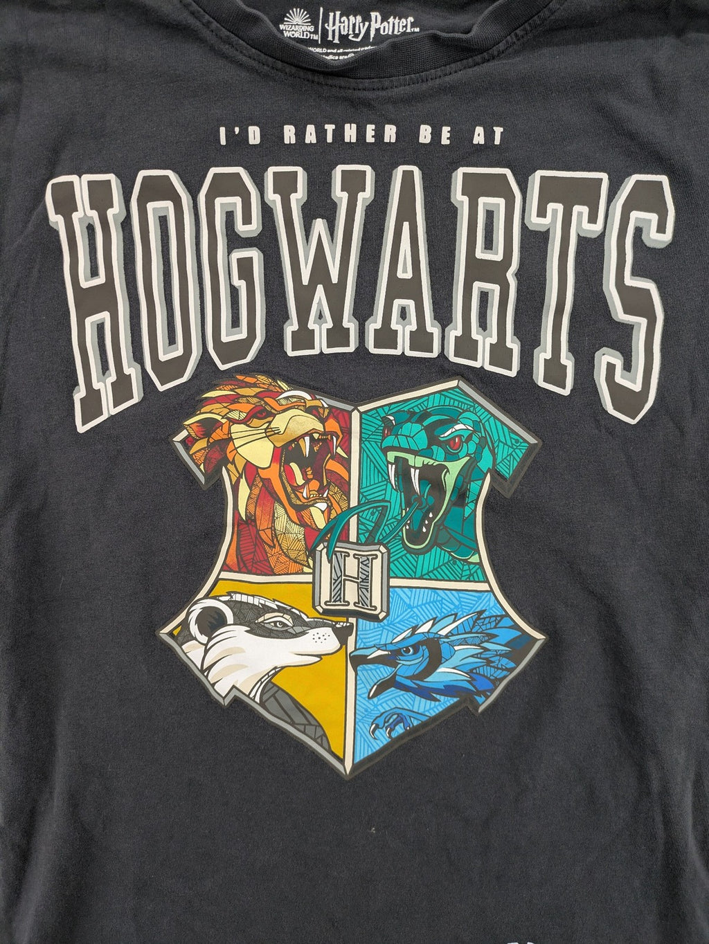 Harry Potter blue t-shirt featuring colorful Hogwarts crest and "I'd Rather Be At Hogwarts" slogan.