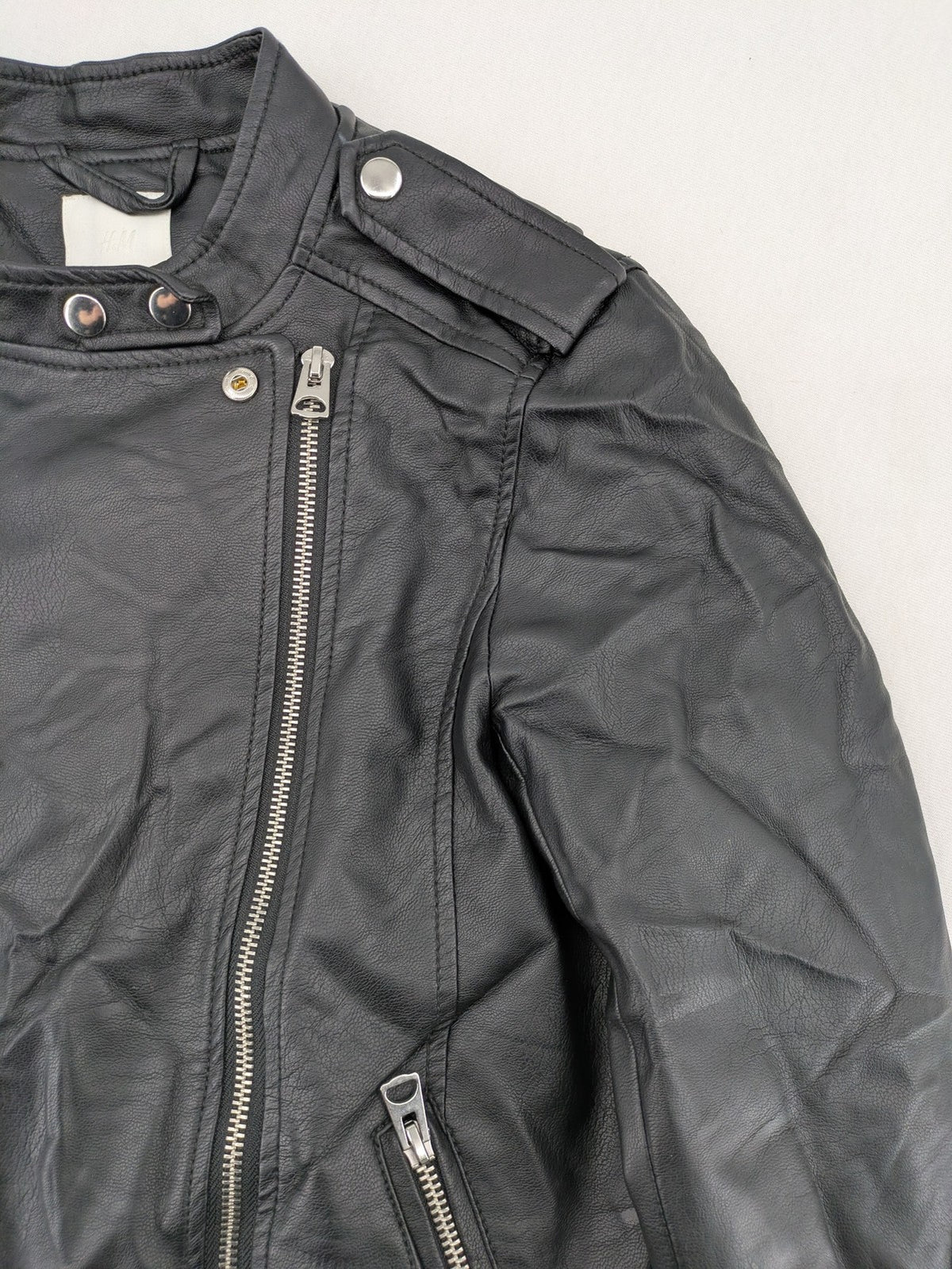 H&M black biker jacket with silver zippers, shoulder flaps, and snap-button details.