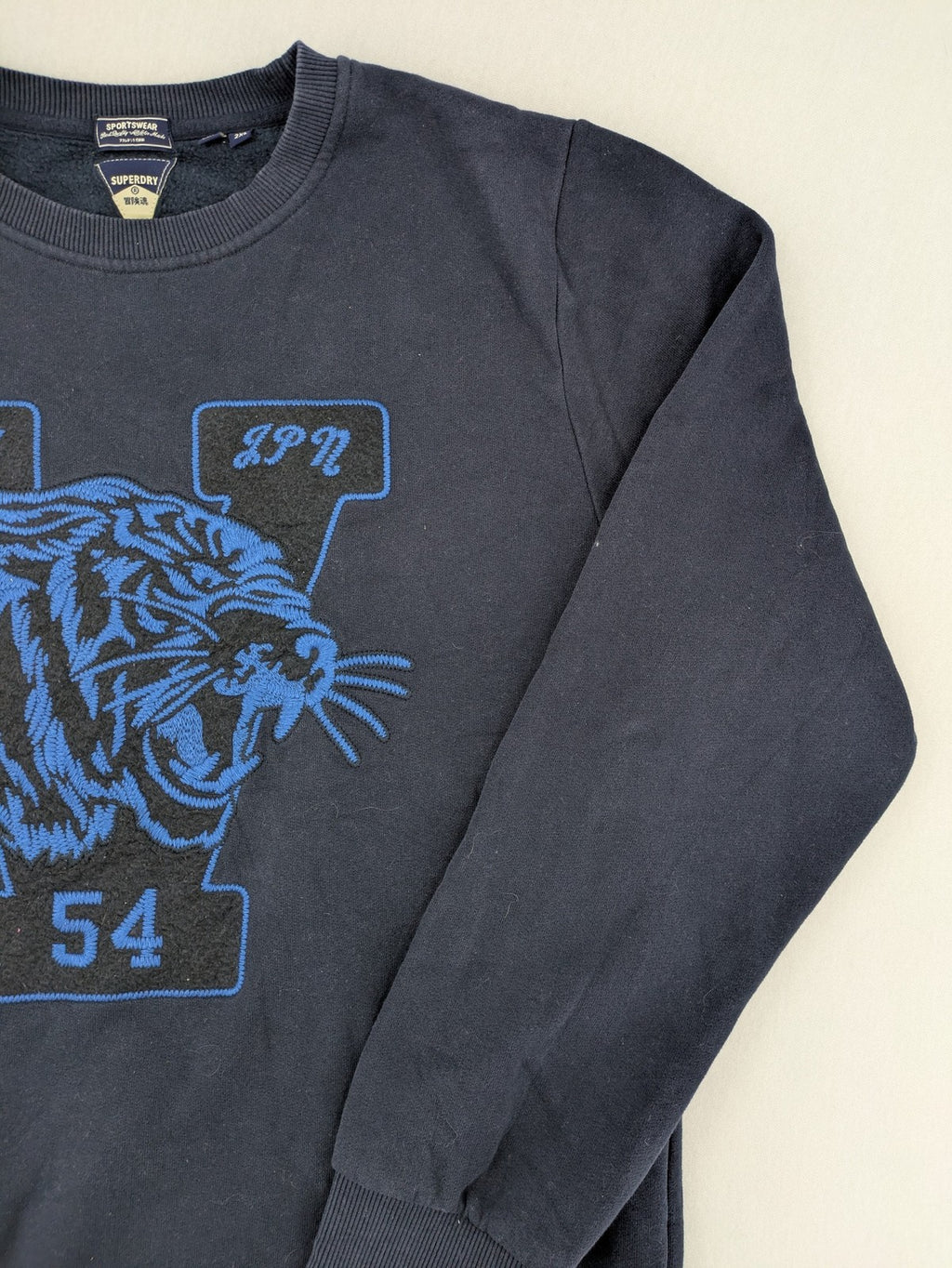 Superdry navy sweatshirt with embroidered tiger graphic and "JPN 54" chenille detail.