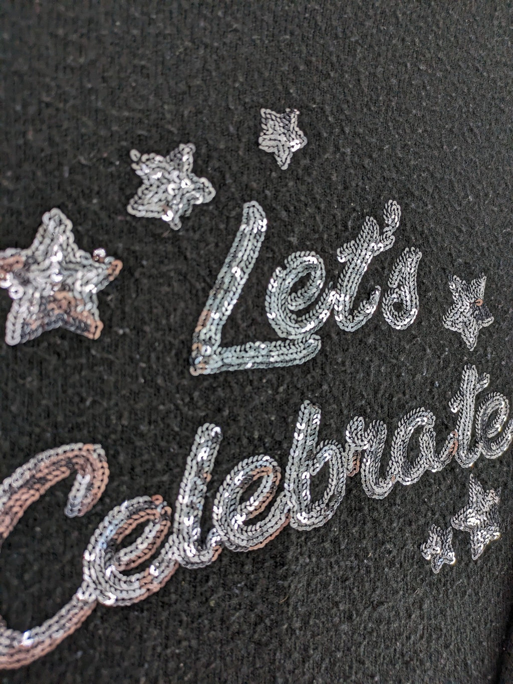 Yessica black turtle neck jumper with sequin "Let's Celebrate" graphic and star details.