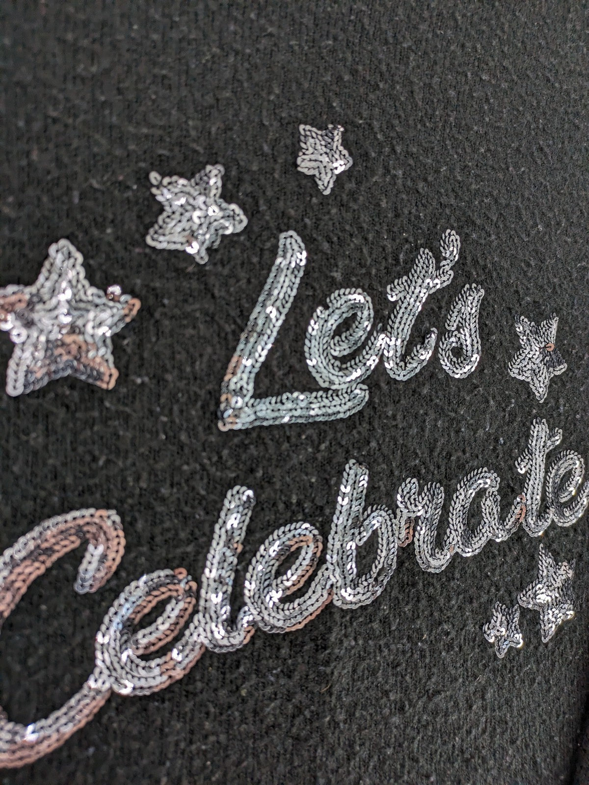 Yessica black turtle neck jumper with sequin "Let's Celebrate" graphic and star details.
