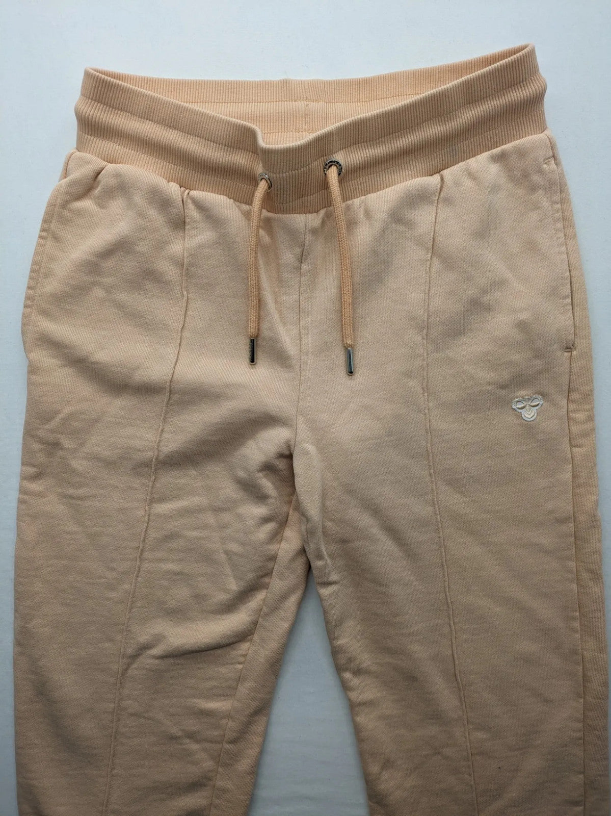Hummel beige jogging pants with adjustable drawstring, embroidered logo, and ankle cuffs.