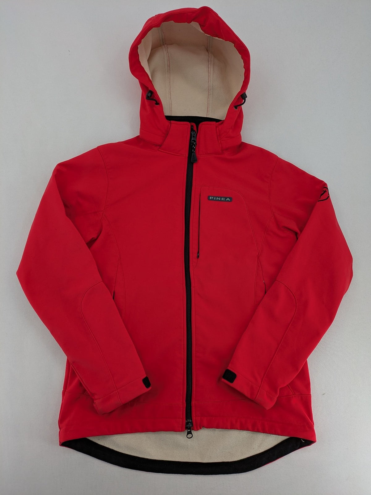 Pinea red softshell jacket with adjustable hood and fleece lining, multiple zippered pockets.