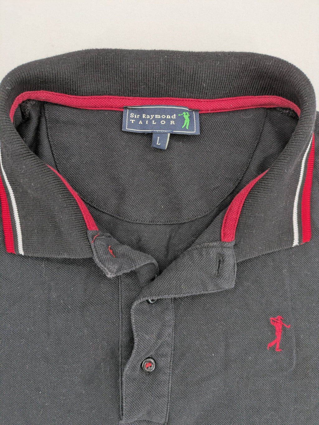 Sir Raymond Tailor black polo shirt with red and white striped collar, embroidered golfer logo.