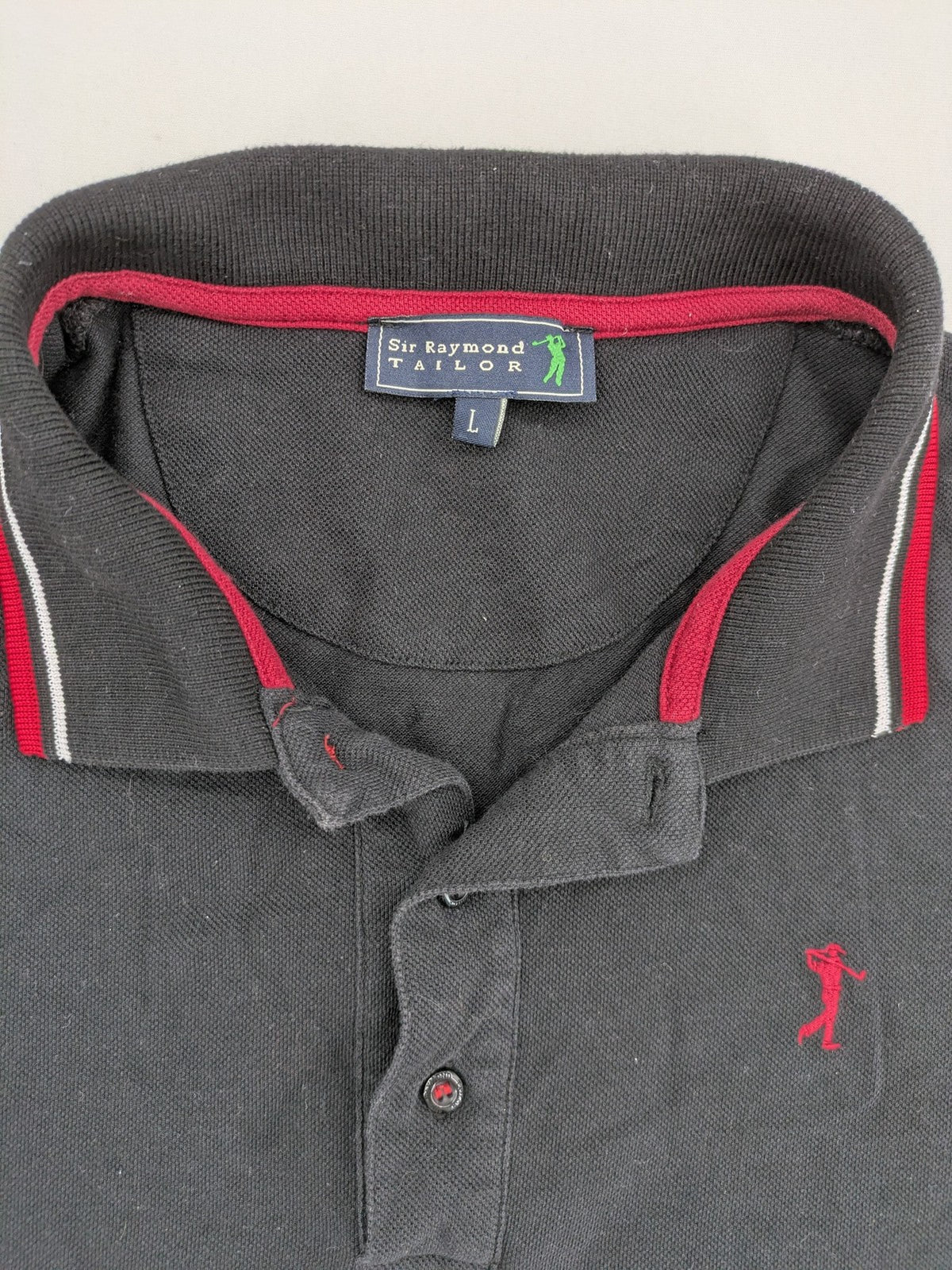 Sir Raymond Tailor black polo shirt with red and white striped collar, embroidered golfer logo.
