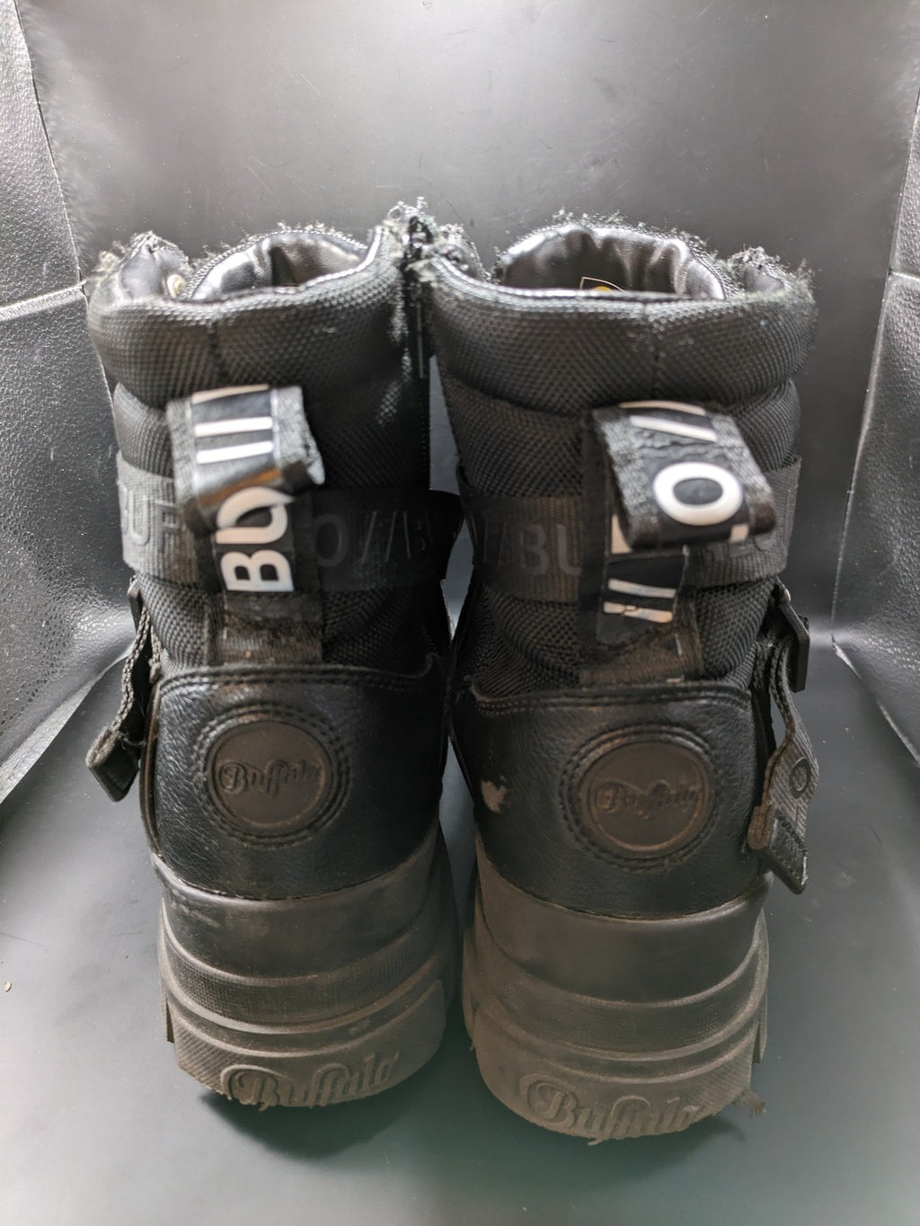 Buffalo black motorcycle boots with chunky sole, adjustable buckle strap, and red plaid lining.
