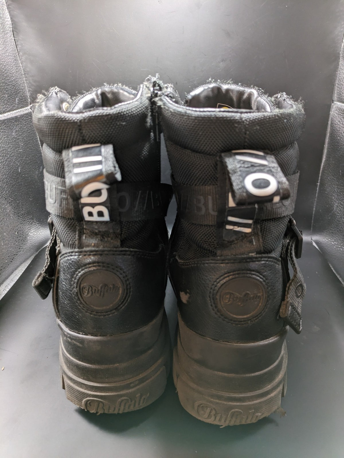 Buffalo black motorcycle boots with chunky sole, adjustable buckle strap, and red plaid lining.
