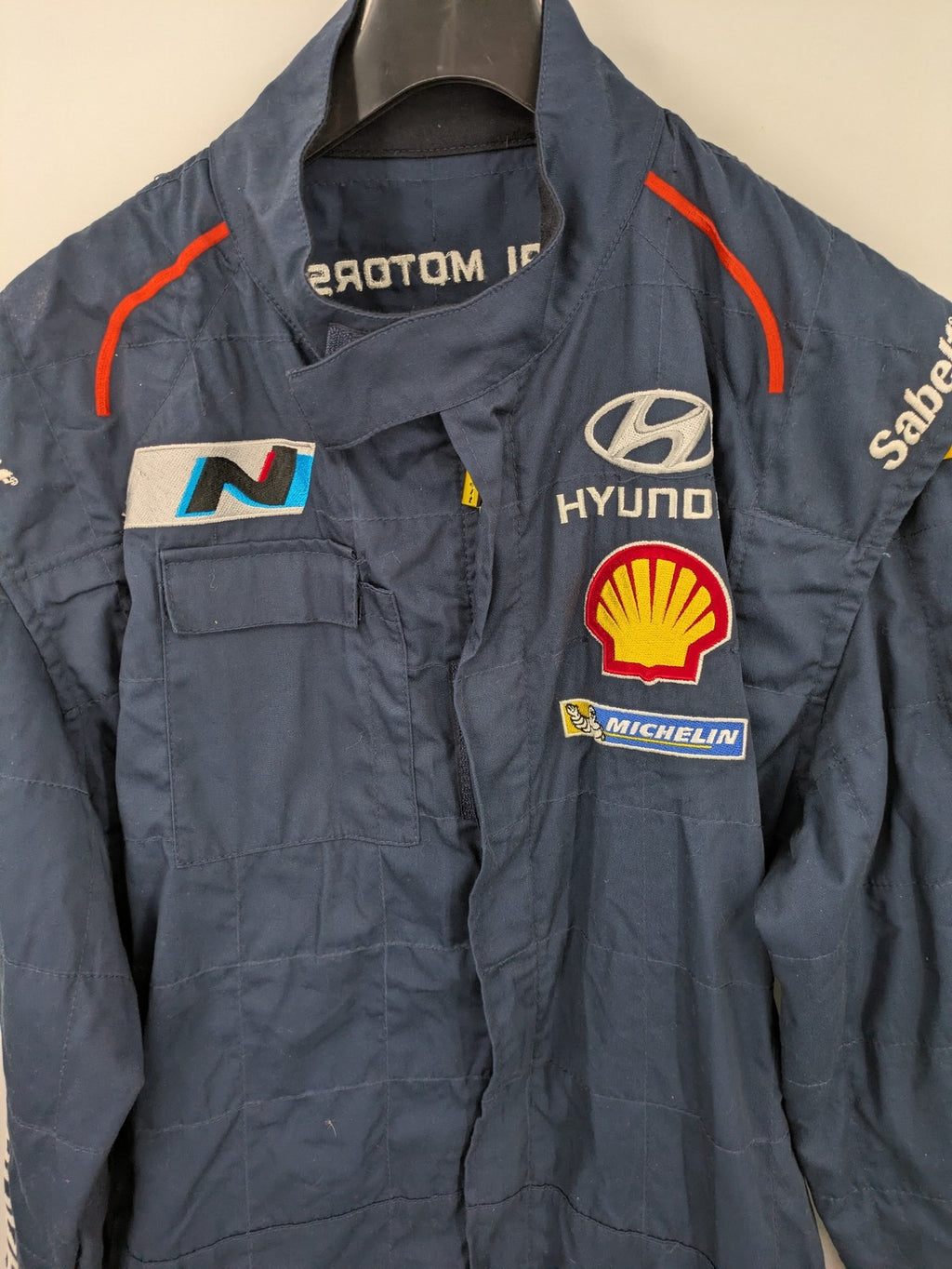 Hyundai Motorsport Sabelt racing suit navy blue with embroidered Shell and Michelin logos.
