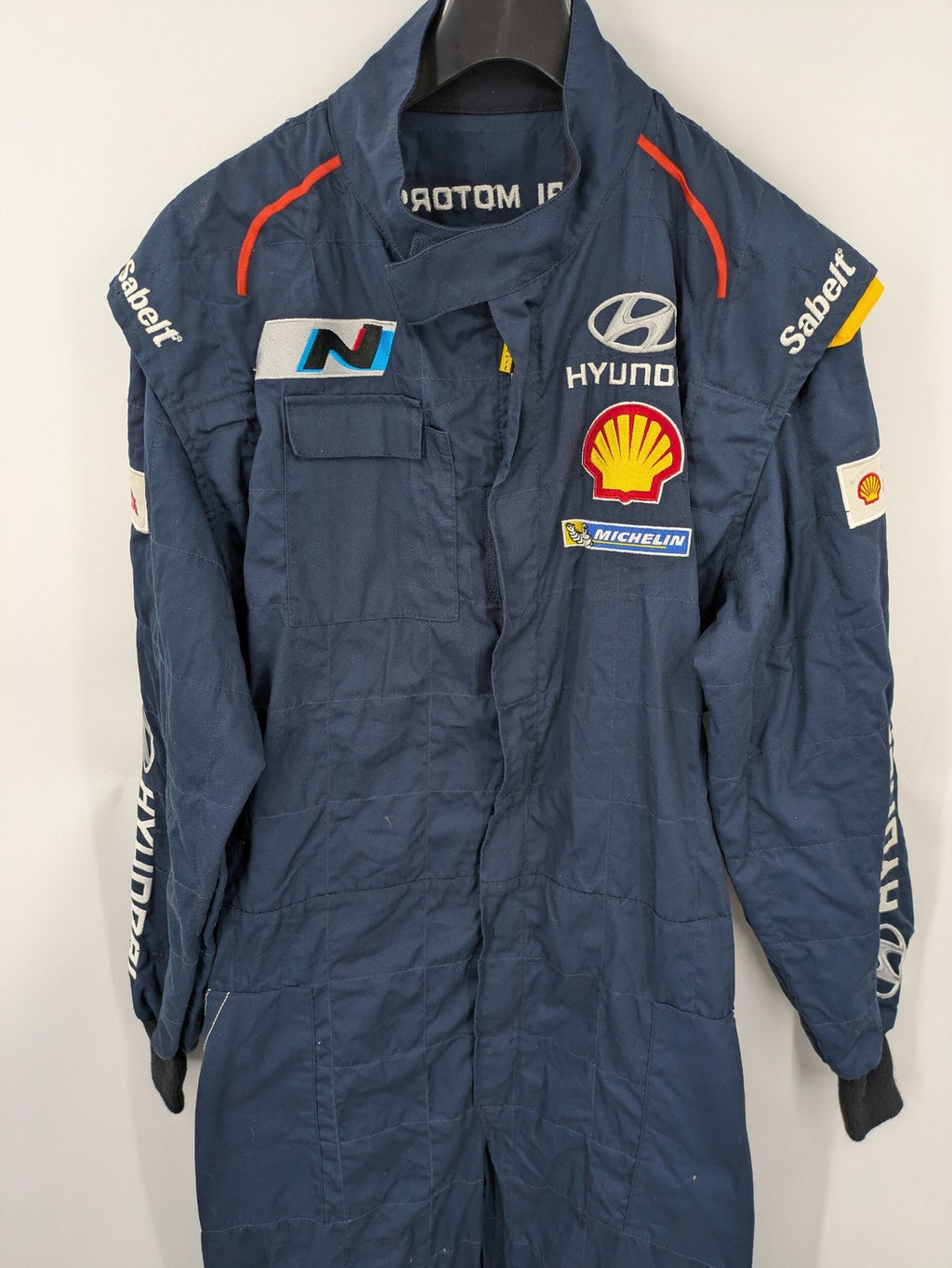 Hyundai Motorsport Sabelt racing suit navy blue with embroidered Shell and Michelin logos.