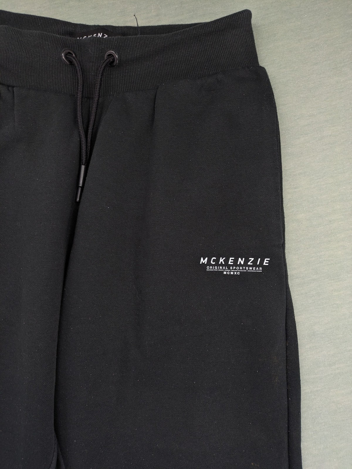 McKenzie black joggers with white logo, tapered fit, and ribbed ankle cuffs.