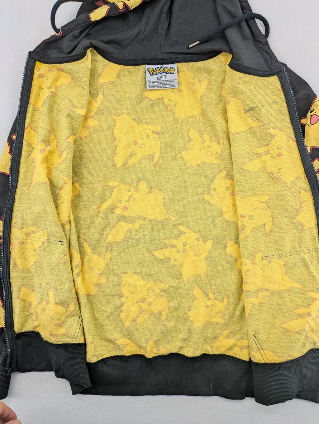 Herren black zip-through hoodie with vibrant Pikachu allover print and yellow lining.