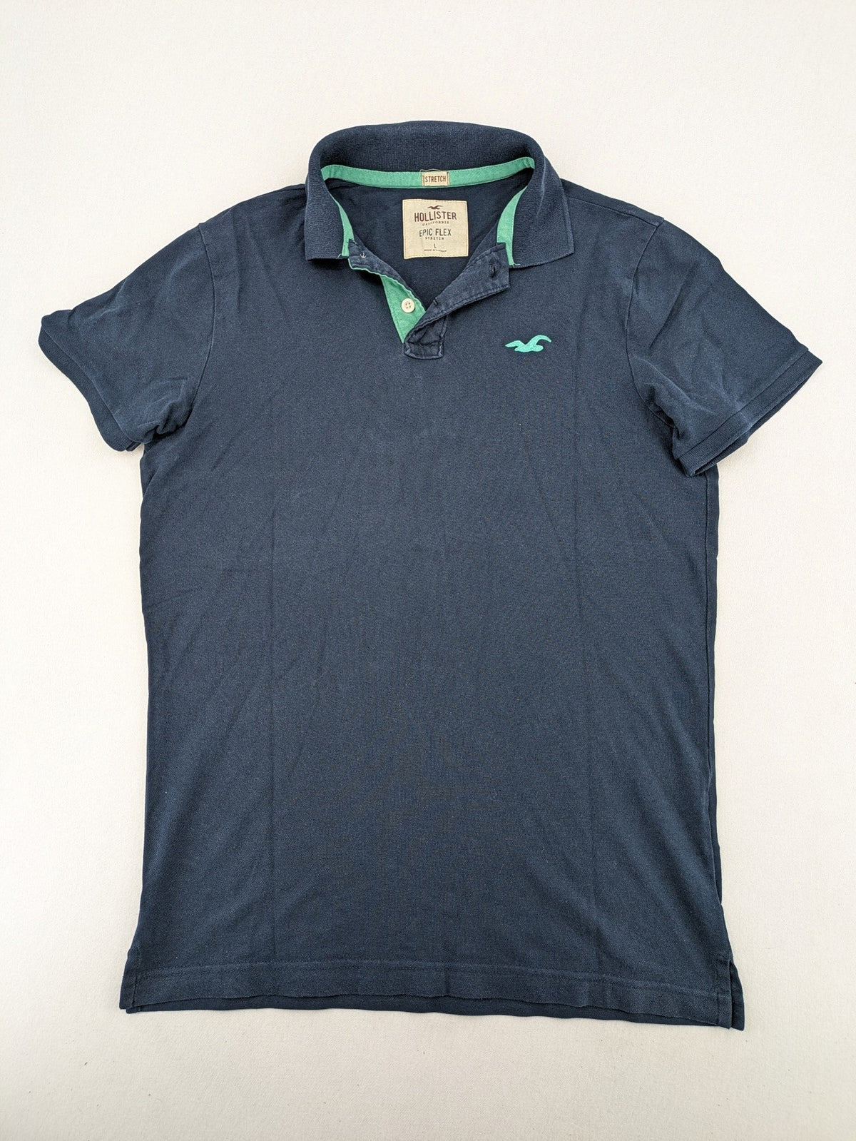 Hollister polo shirt navy blue with embroidered seagull logo and green trim.