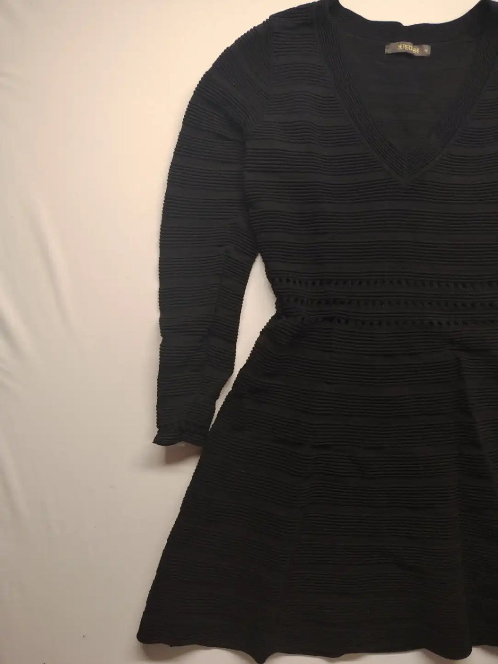 Supertuga black ribbed dress with V-neck, long sleeves, and pointelle detail at waist.
