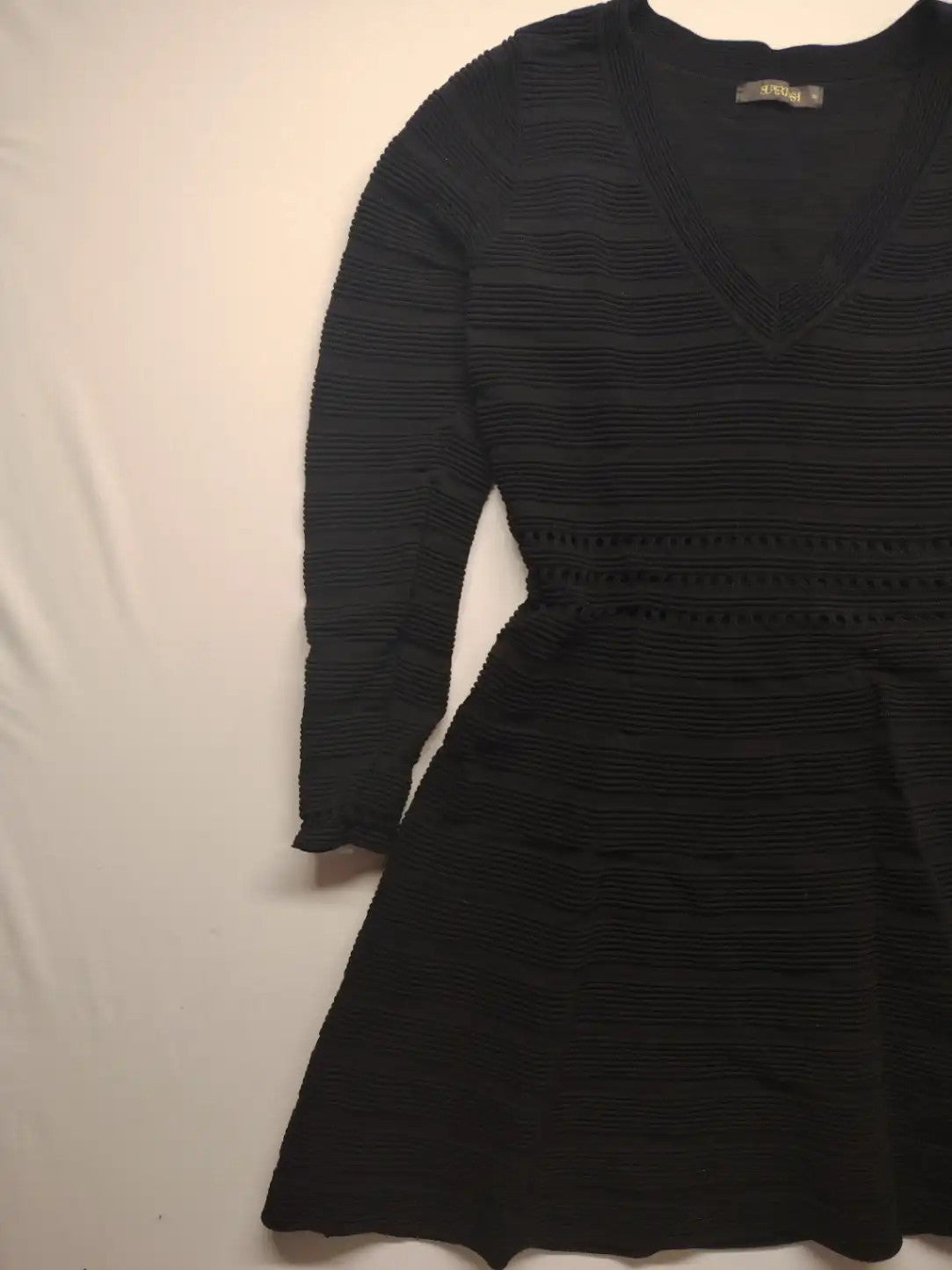 Supertuga black ribbed dress with V-neck, long sleeves, and pointelle detail at waist.
