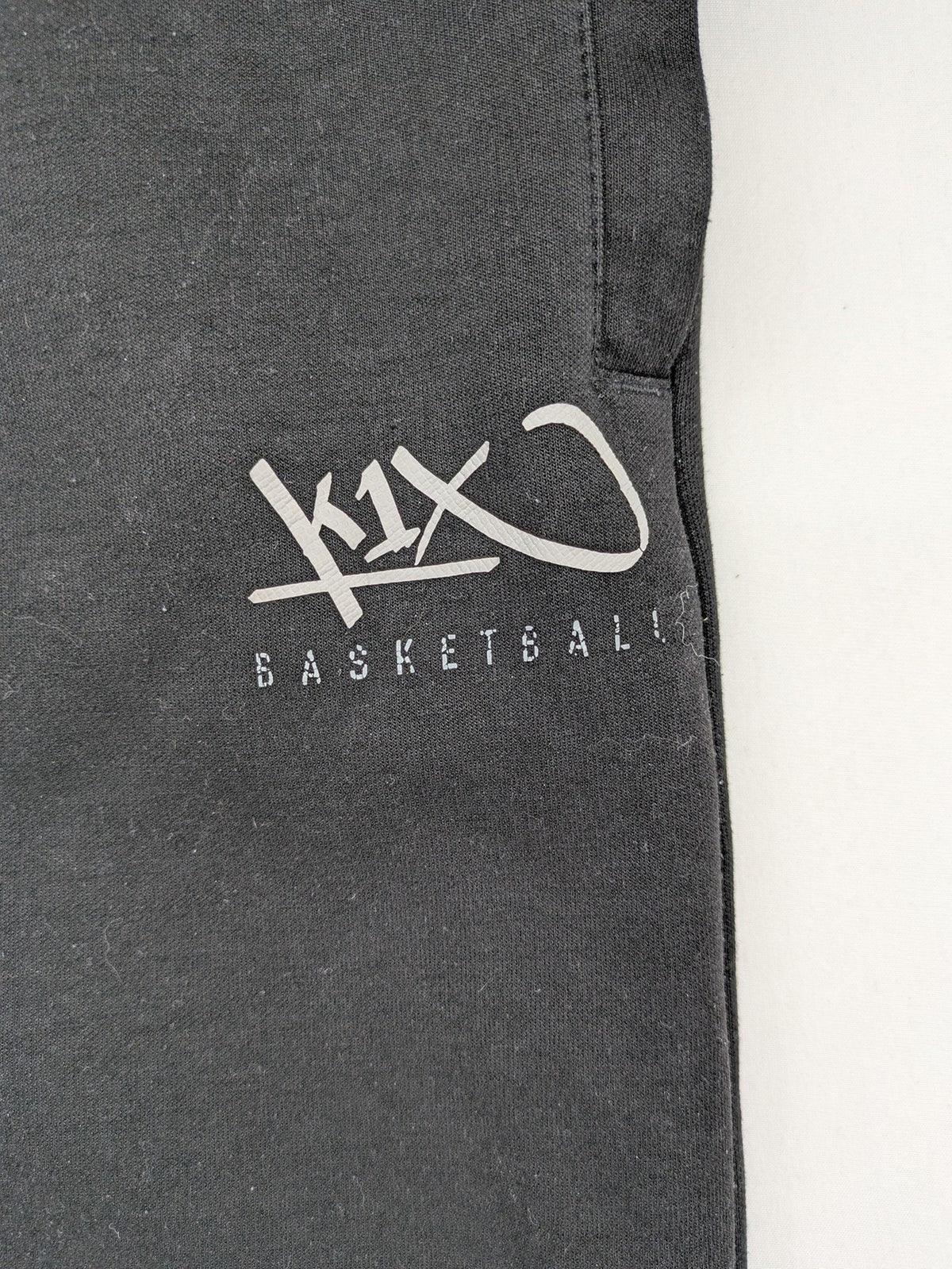 K1X grey joggers with white basketball logo, elastic waistband, and cuffed ankles.