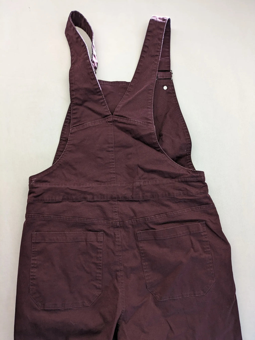 Kazane burgundy overalls with adjustable straps, side button placket, and chest pocket.