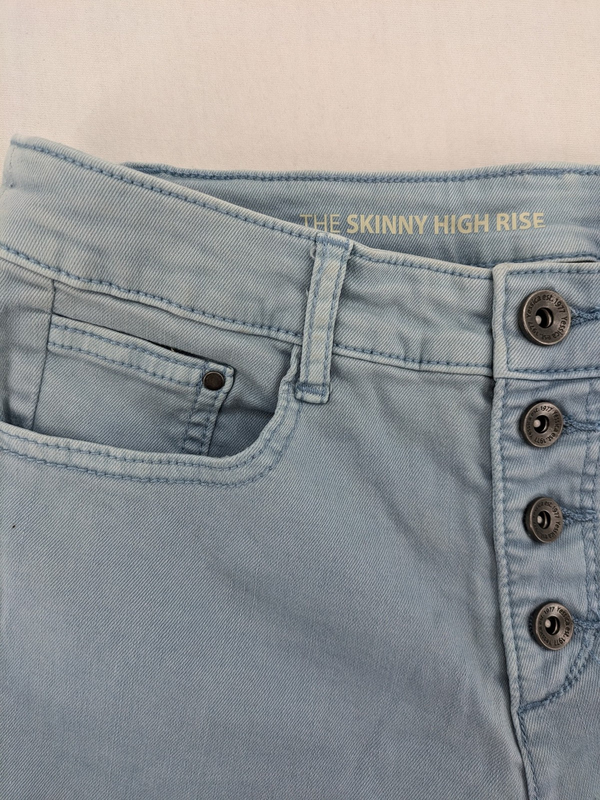 Yessica blue skinny jeans high rise with button fly and V-cut hem detail.