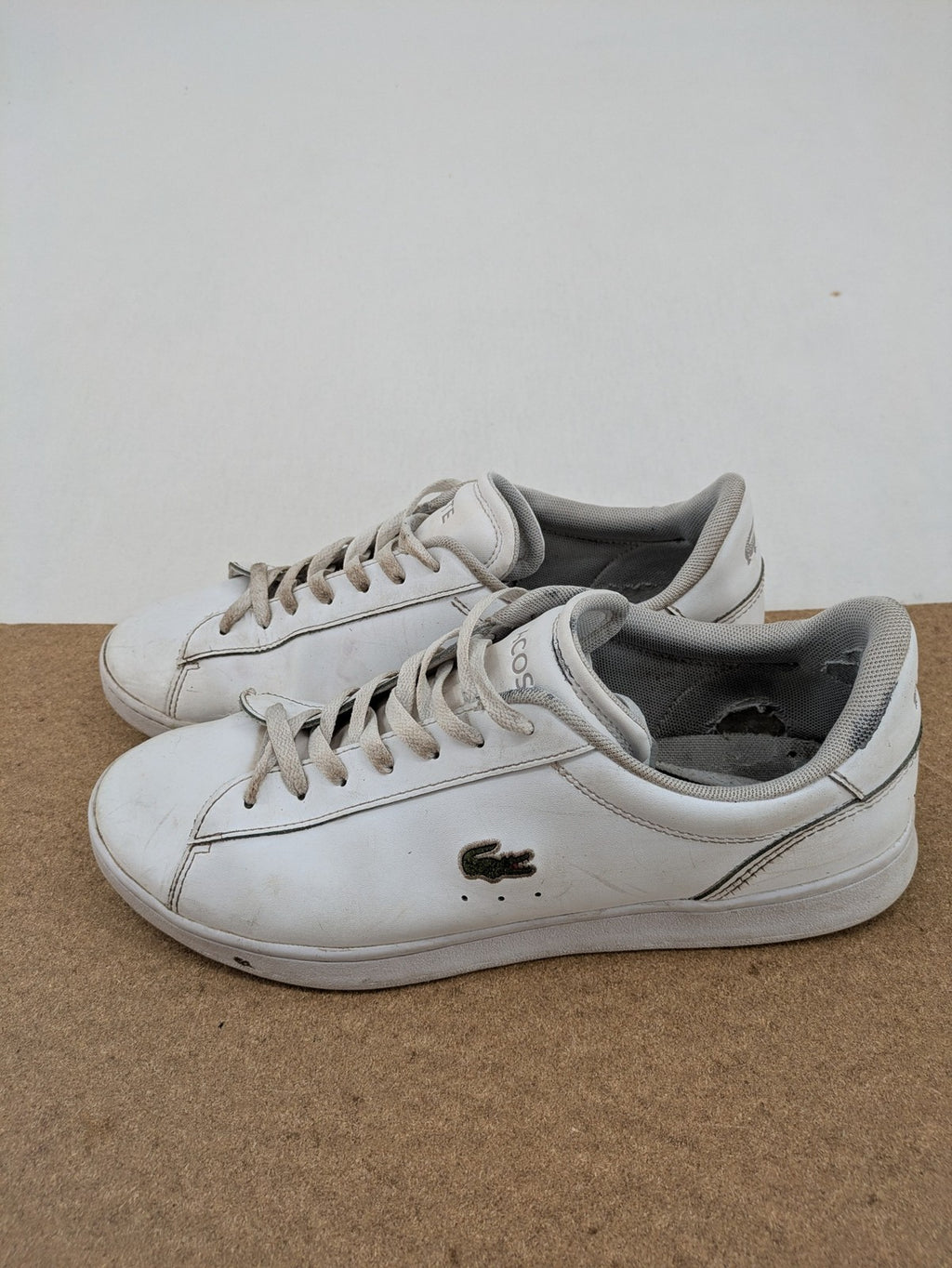 Lacoste cream low top sneakers with iconic crocodile logo and classic design.