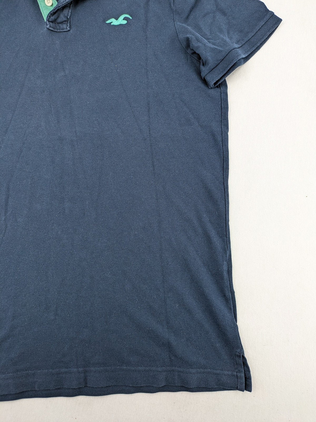 Hollister polo shirt navy blue with embroidered seagull logo and green trim.