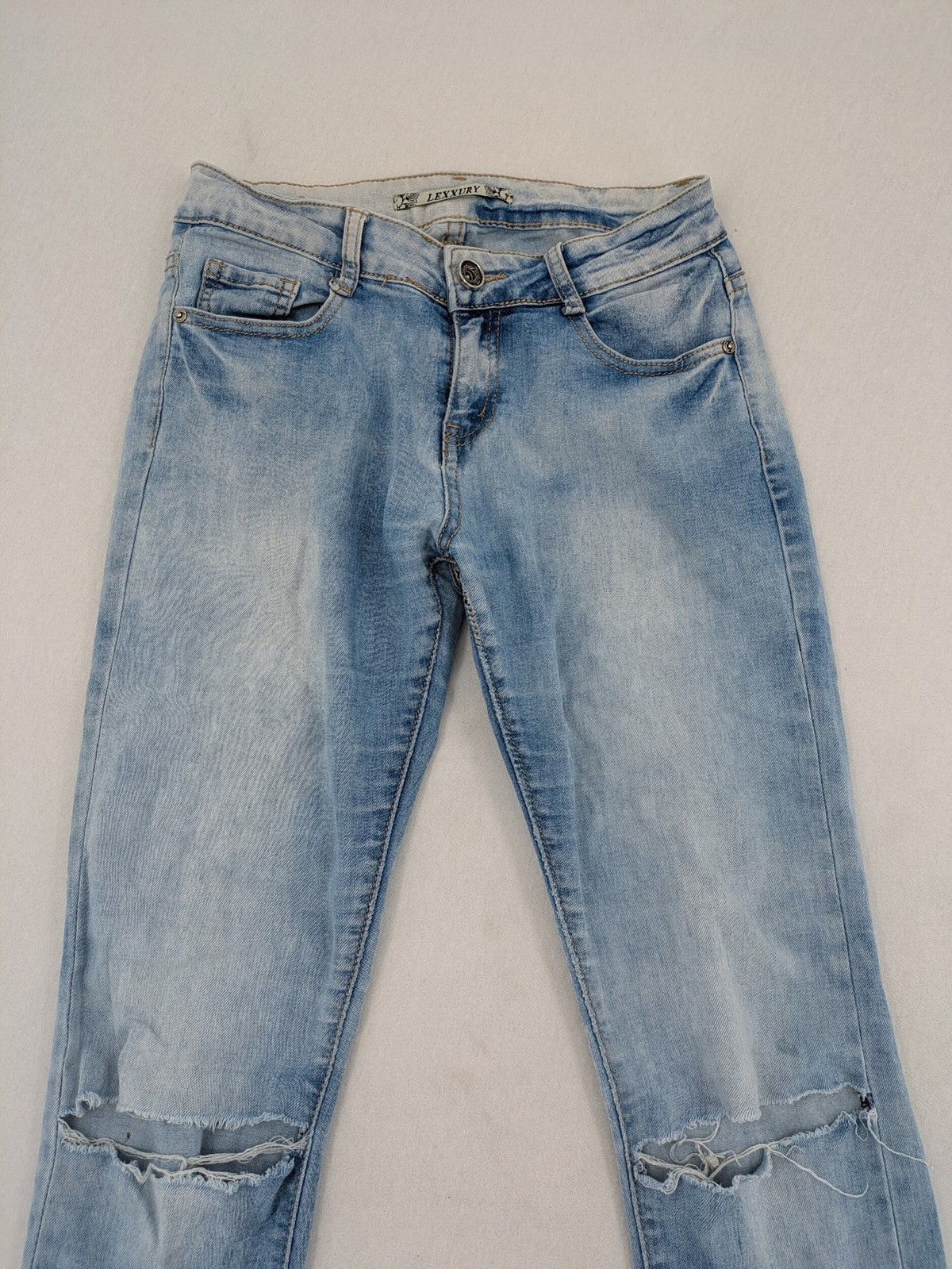 Lexxury blue skinny jeans distressed with knee rips and light wash finish.