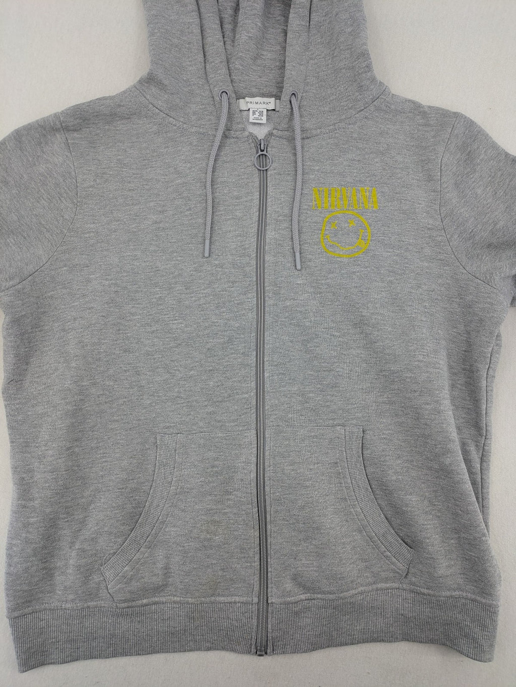 Primark grey zip-through hoodie featuring yellow Smiley logo and Nevermind graphic.