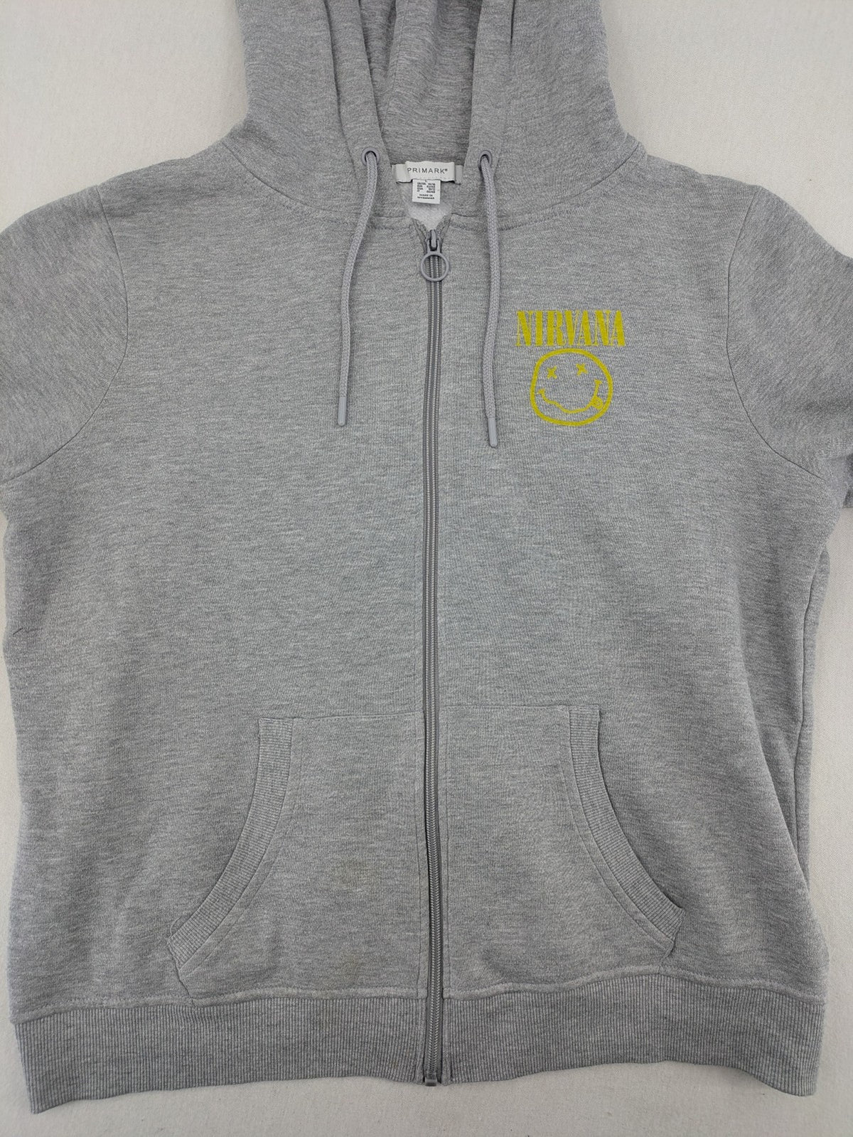 Primark grey zip-through hoodie featuring yellow Smiley logo and Nevermind graphic.