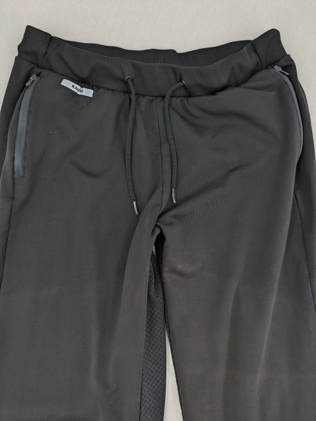 Kalenji black loungewear pants with grey accents and zippered side pockets.