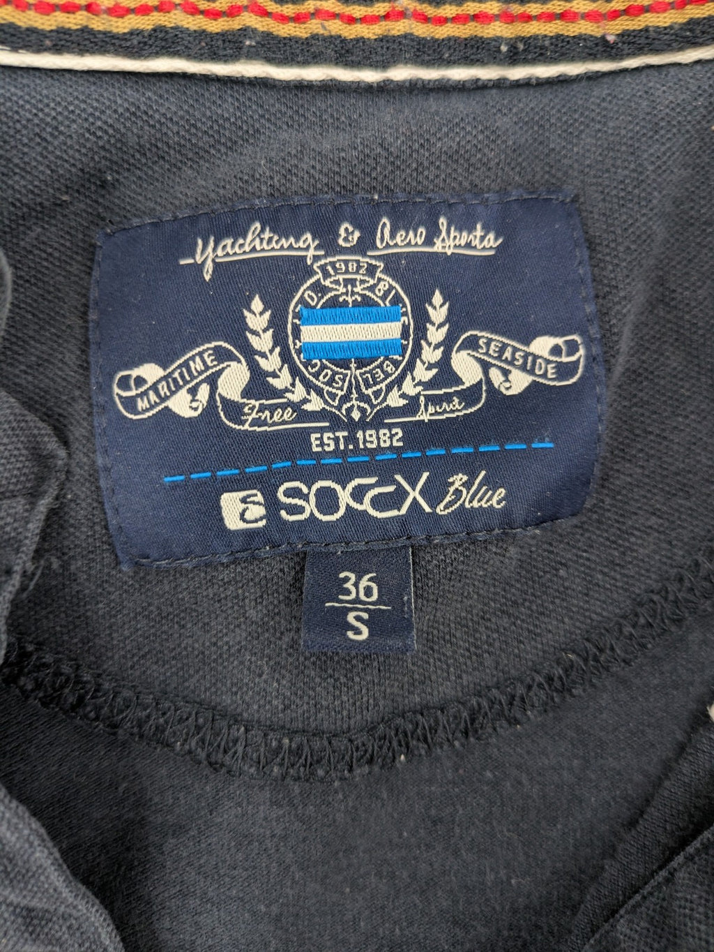 Soccx blue polo shirt with British Columbia graphic, embroidered patches, and striped collar.