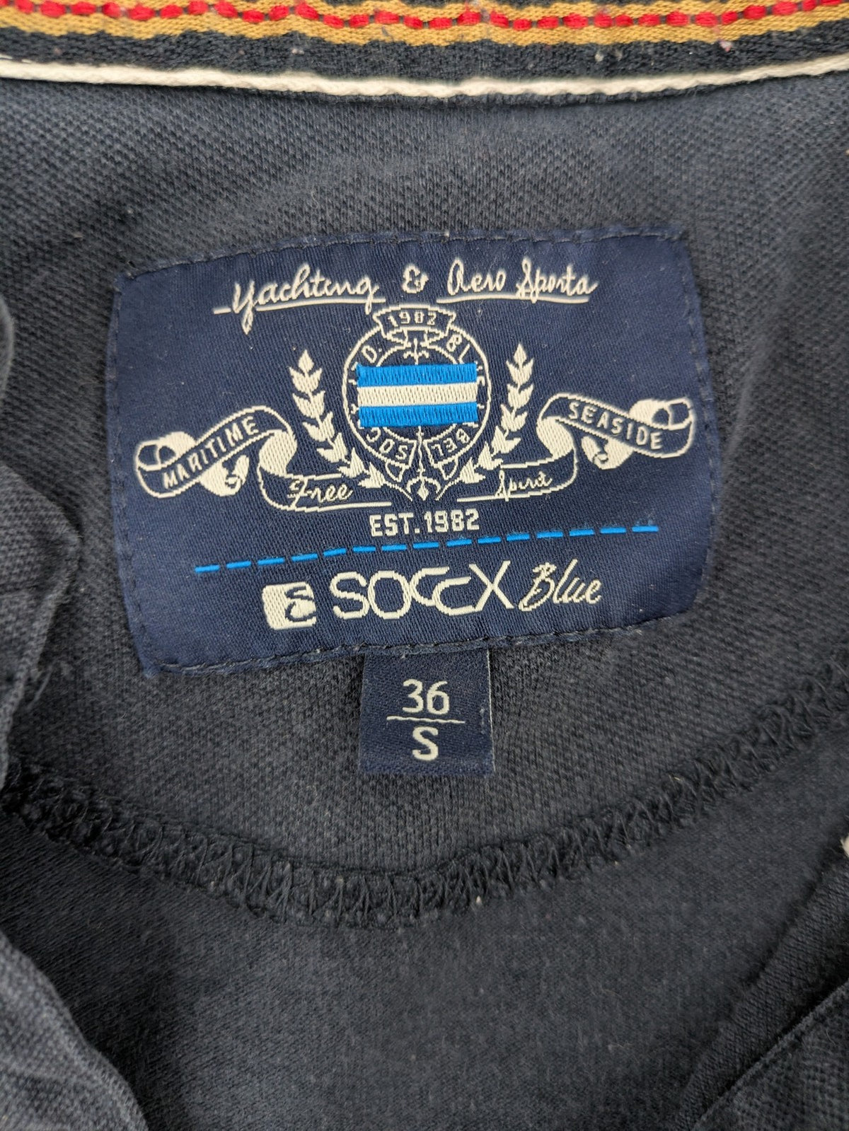 Soccx blue polo shirt with British Columbia graphic, embroidered patches, and striped collar.