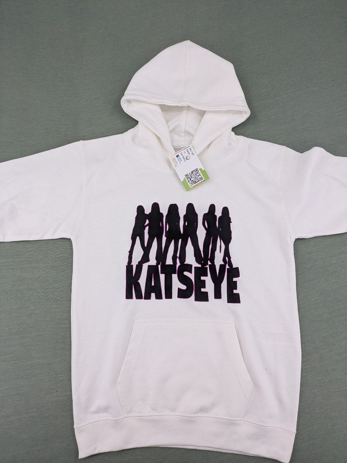 KATSEYE white zip-through hoodie with black silhouette graphic and logo, classic pullover style.